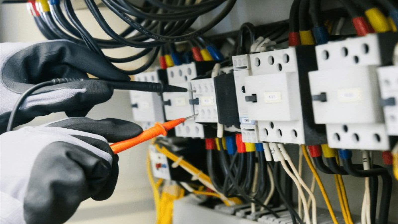 Electrician in gloves testing wiring with probes inside an electrical control panel